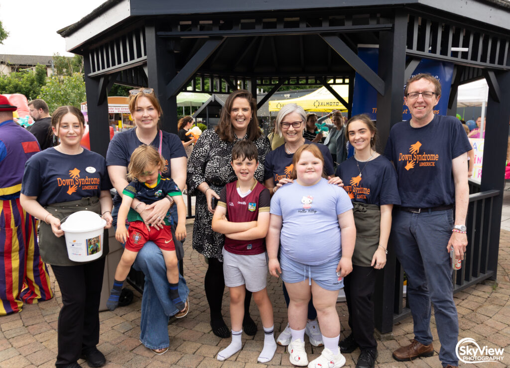 A group of adults and children pose together outside a gazebo at an outdoor event, some wearing Down Syndrome Limerick shirts.
